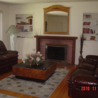 A cozy living room with a fireplace, leather sofas, and a central coffee table, surrounded by built-in shelves and a mirror above the mantel.