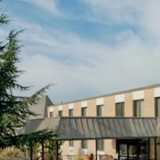 A modern hotel building with large windows under a blue sky, surrounded by trees.