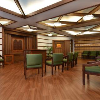 A modern conference room with wooden paneling, green chairs, and bookshelves.