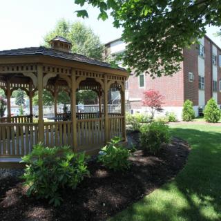 A beautiful garden scene with a wooden gazebo surrounded by lush greenery and well-manicured landscaping.