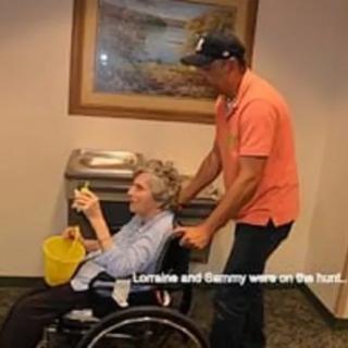 A man assists a senior in a wheelchair indoors.
