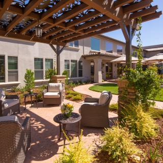 A beautifully landscaped outdoor patio area featuring a pergola, comfortable seating, and lush greenery.