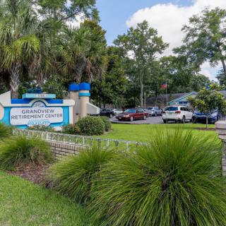 A view of a school entrance with a sign, surrounded by lush greenery and a parking lot filled with cars.