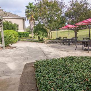 A paved patio area with outdoor seating and pink umbrellas, surrounded by lush landscaping.