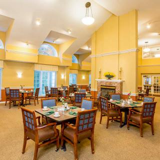 A spacious, elegantly decorated dining room with tables and chairs arranged neatly, featuring a warm color scheme and a central fireplace.