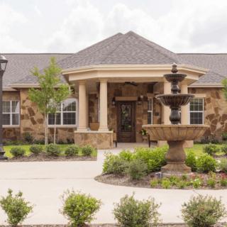 A beautiful stone house with a landscaped garden and a fountain in the driveway.