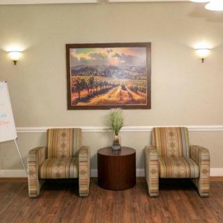 A cozy waiting area with two striped chairs, a central table with a plant, and a landscape painting on the wall.