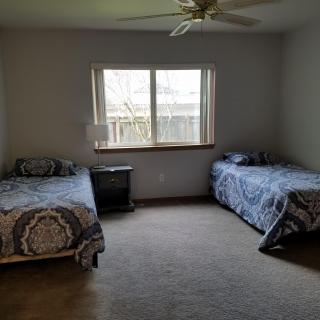 A minimalist bedroom with two twin beds, a window, and a ceiling fan.