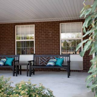 A cozy porch featuring two benches adorned with colorful cushions alongside a brick wall and windows.