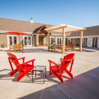A sunny outdoor courtyard featuring red chairs and a wooden pergola.