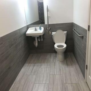 A clean and modern bathroom with a toilet, sink, and mirror, featuring accessibility features like grab bars.