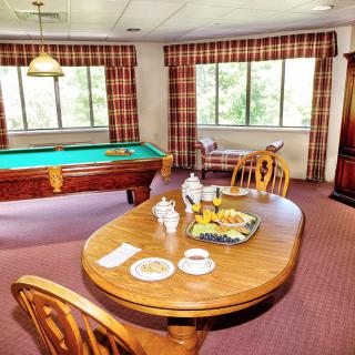 A cozy room with a billiards table and a dining area, featuring large windows with plaid curtains.