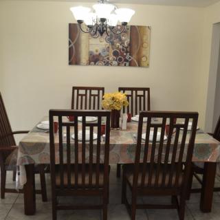 A neatly arranged dining room with a table, chairs, and a chandelier, accented by artwork and a floral centerpiece.