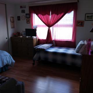 A cozy bedroom with a bed near the window, red curtains, and various furniture pieces.