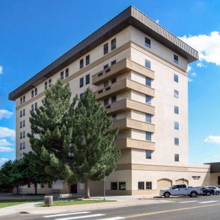 A multi-story residential apartment building with trees in the foreground, set against a clear blue sky.