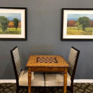 A small chess table with two chairs, framed by landscape paintings on the wall.