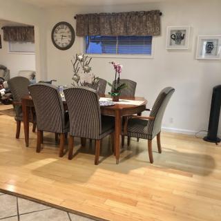A cozy dining room with a wooden table and elegant chairs, complemented by a wall clock and decorative plants.