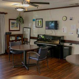 A cozy communal room featuring a piano, television, tables, and chairs with various decorations on the walls.