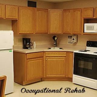 A kitchen setup used for occupational rehabilitation, featuring essential appliances and wooden cabinets.