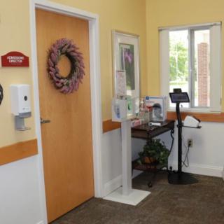 A welcoming entrance with a wreath-adorned door, hand sanitizer, and a small table by the window.