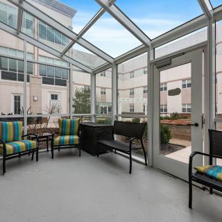 A glass-enclosed patio area with colorful chairs and tables in front of an apartment building.