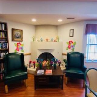 A cozy living room with two green armchairs facing a fireplace, surrounded by colorful decorations and a wooden bookshelf.