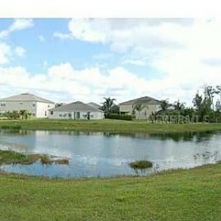A suburban neighborhood featuring houses surrounding a small pond under a partly cloudy sky.