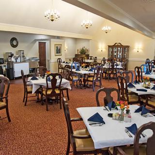 An elegant dining room with neatly arranged tables and chairs, decorated with blue napkins and warm lighting.