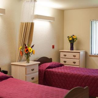 A cozy bedroom with two beds covered in red bedding and decorated with vases of flowers on the dressers.