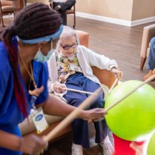 A healthcare worker engages an elderly person in a balloon activity at a nursing home.