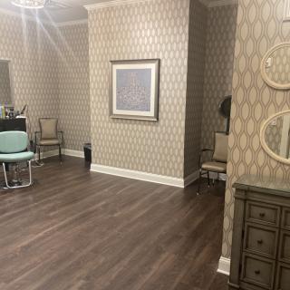 A elegantly decorated room featuring patterned wallpaper, wooden flooring, and various furniture pieces including chairs and mirrors.