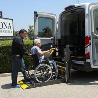 A person in a wheelchair being assisted onto a van using a lift ramp.