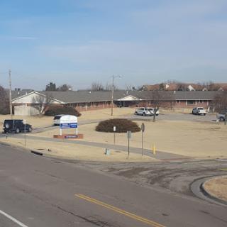 A view of a building complex with vehicles parked in an open area under a clear sky.