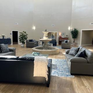 A modern lobby features comfortable seating around a central fountain, complemented by indoor plants and a high ceiling.