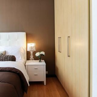 A cozy bedroom with a warm color scheme featuring a bed, nightstand with lamp, and built-in wardrobe.