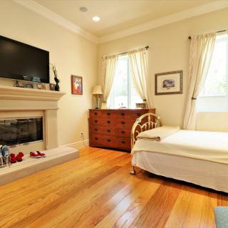Cozy bedroom with a fireplace and television, featuring wooden flooring and natural light from two windows.