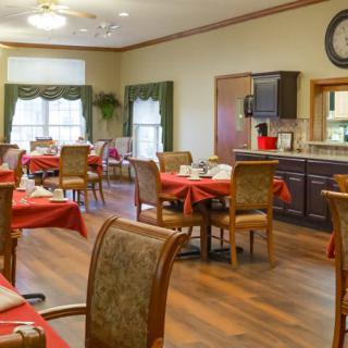 A cozy dining room with red tablecloths and a small kitchen area.