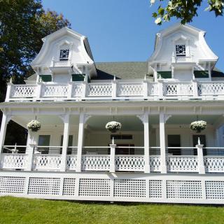 A charming white Victorian house with a spacious porch and hanging plants.