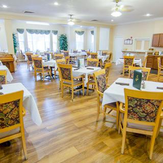A bright dining room with neatly arranged tables and chairs, featuring wood flooring and large windows.