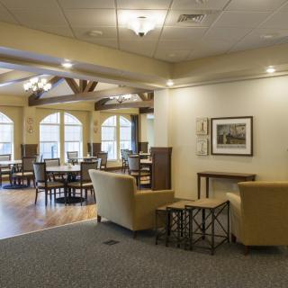 A cozy interior lounge area featuring comfortable seating and dining tables, illuminated by natural light through large windows.