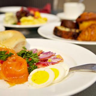 A delicious breakfast spread featuring smoked salmon, hard-boiled eggs, and a bagel with a side of pastries and coffee.