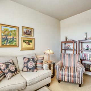 Cozy living room with a sofa and armchair, decorated with paintings and a bookshelf.