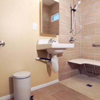 An accessible bathroom with a wall-mounted sink, shower area with a seat, and grab bars for support.