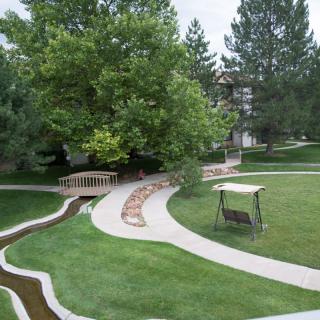A serene garden scene with winding pathways, a small bridge, and a swing amidst lush greenery.