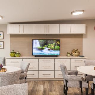 A modern living space featuring white cabinets, a TV, and comfortable seating around round tables.