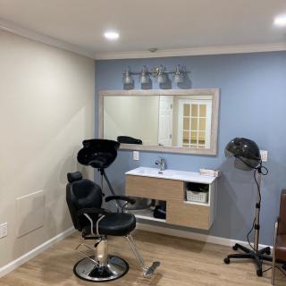 A modern hair salon setup with a barber chair, sink, mirror, and drying hood.