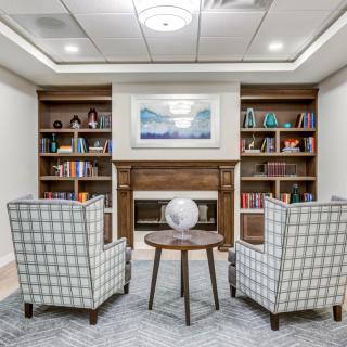 A cozy library with two armchairs facing a fireplace, surrounded by bookshelves and a small coffee table holding a globe.
