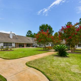 A residential property with a well-maintained lawn and trees, featuring a pathway leading to the house.