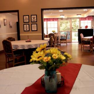 A cozy dining area with tables and chairs, adorned with a centerpiece of yellow flowers in a vase.