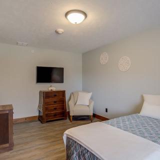 A minimalist bedroom with a bed, dresser, chair, and wall-mounted television.